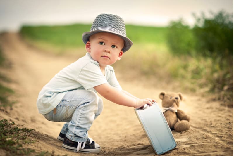 Little boy playing with teddy bear on the footpath