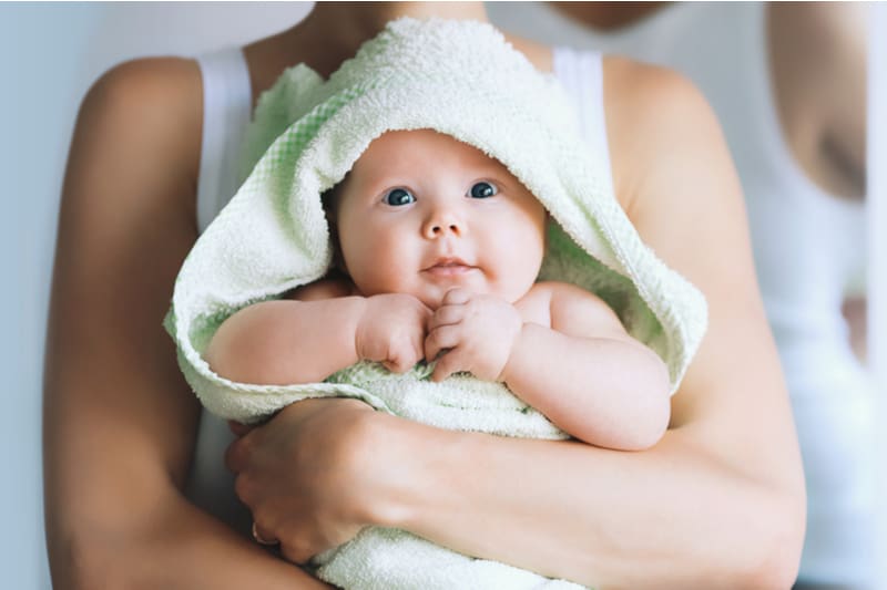 Mom hugs her little baby after bath with towel on head