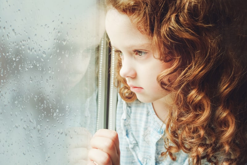 Sad child girl looking out the window