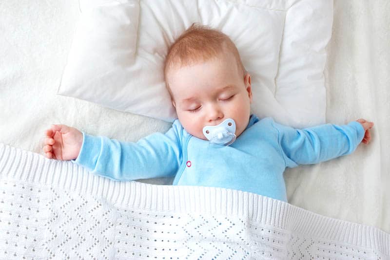 adorable baby with pacifier sleeping on bed covered with blanket