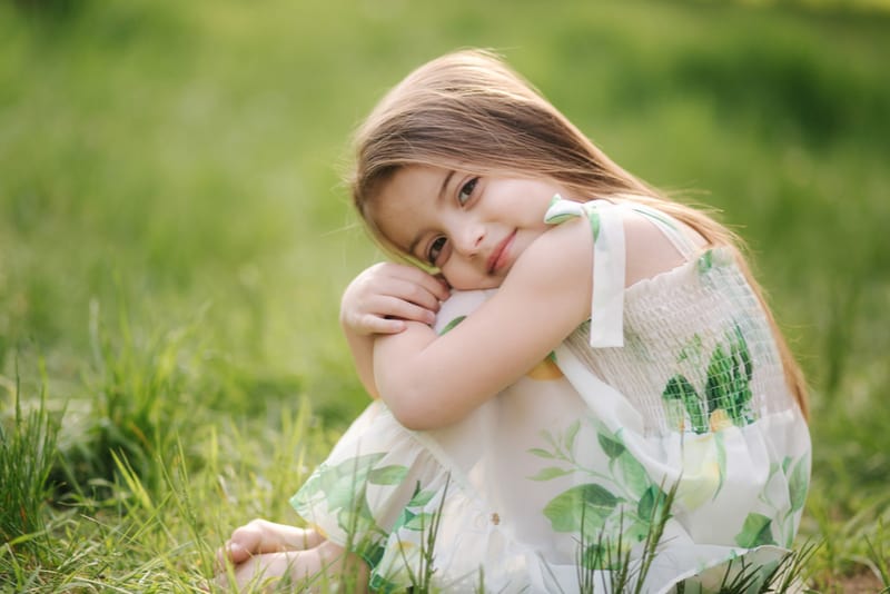 adorable little girl sits barefoot on the grass in the park