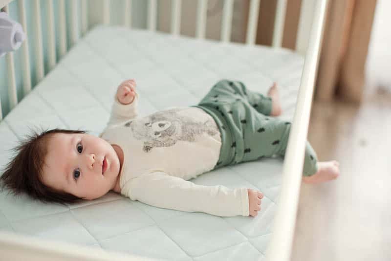 baby boy lying in crib with one leg hanging through the rails