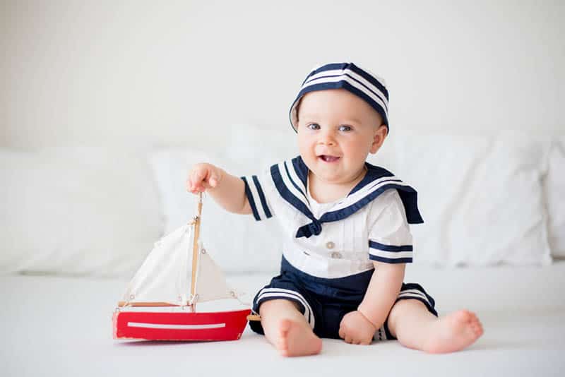 baby boy wearing a sailor clothes and playing with wooden boat on the floor