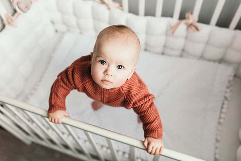 cute baby girl wearing sweater standing in the crib and looking up