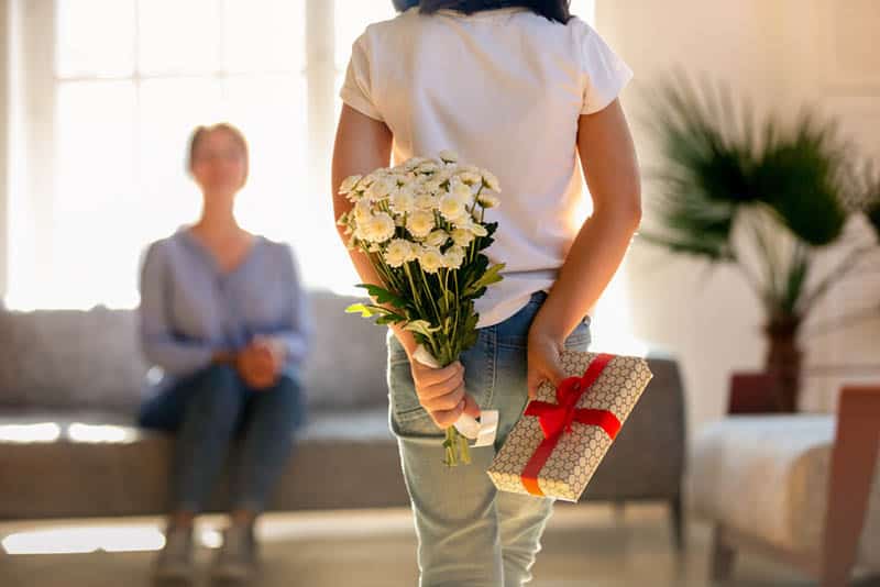 little girl holding gift and flowers as a surprise for mother