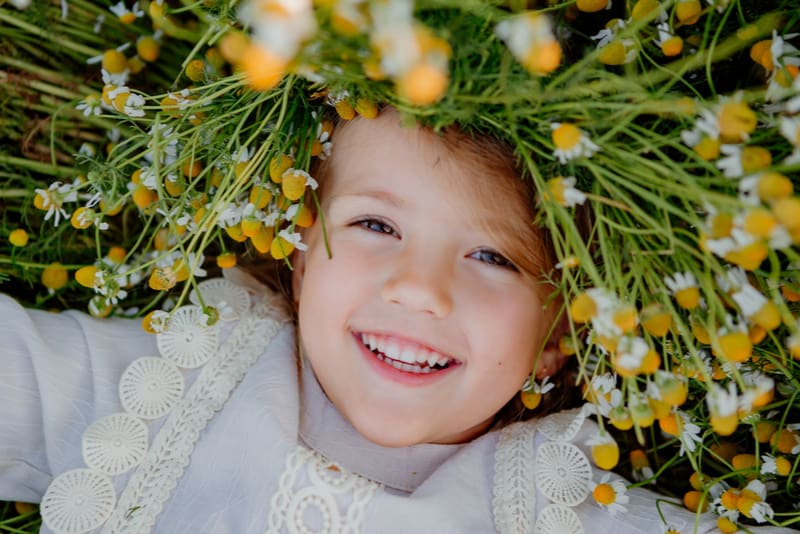 little girl in a cotton dress lies in a field of daisies