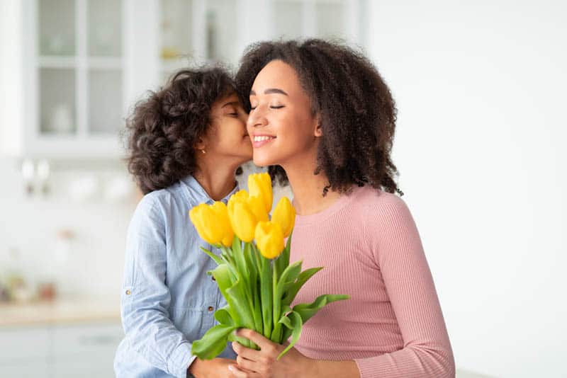 little girl kissing her mother for birthday with flowers