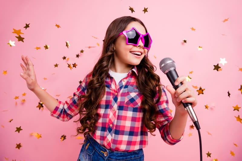 little girl with funny sunglasses singing and dancing in front of a pink background