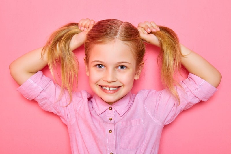 little girl with pigtails smiling in front of a pink background