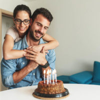 a woman hugs her husband on his birthday and gives him a birthday cake