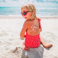 happy little girl sitting on a Hawaiian beach with sunscreen on her back