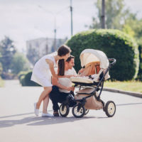 mother and father walk through the park with their daughter in a stroller