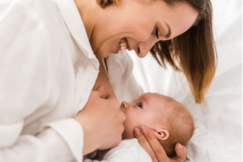 Smiling young mother in white t-shirt breastfeeding baby