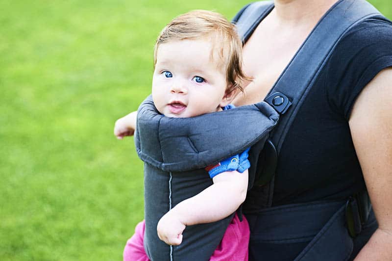 Young mother with her little baby child girl in a carrier outside in nature