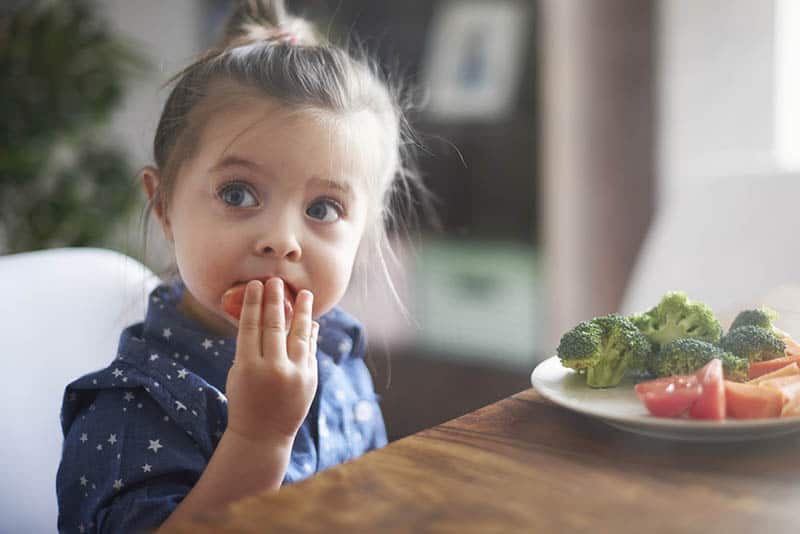 adorable little girl eating vegetables from the plate