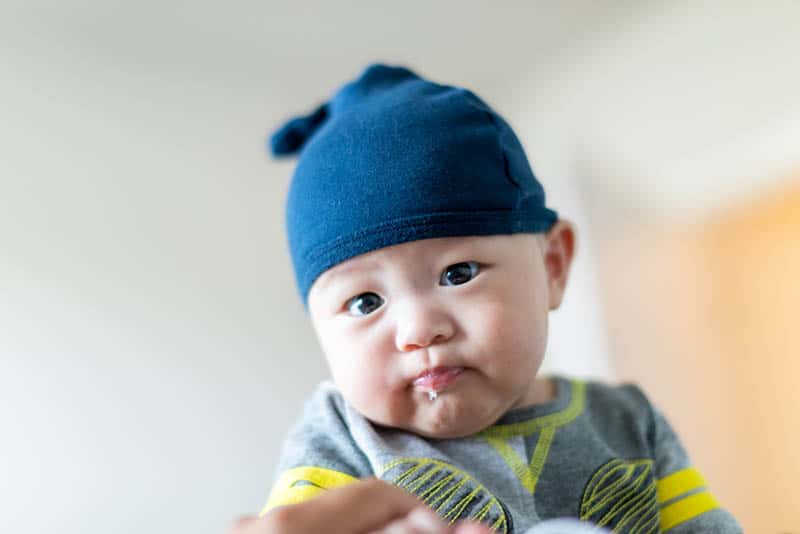 cute baby boy wearing blue hat and spitting up