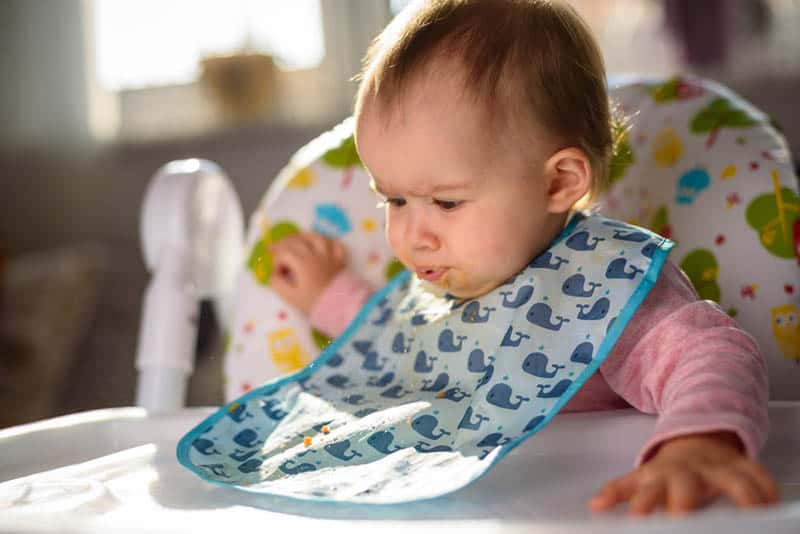 funny baby girl eating in a high chair