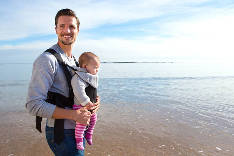 happy father carrying baby in the carrier on the beach
