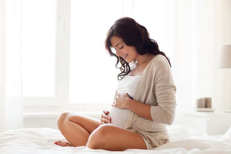 happy pregnant woman sitting on bed