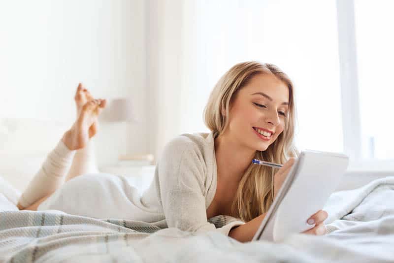 happy young woman with pen and notebook in bed