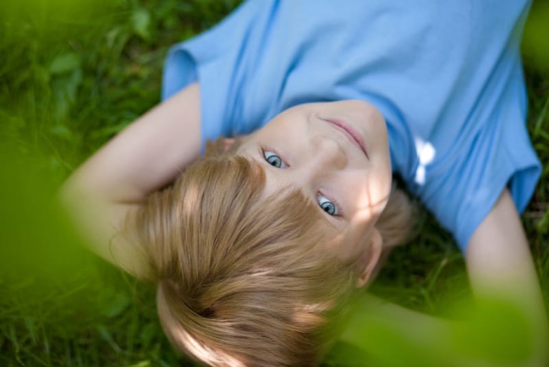 little boy in blue t-shirt lying on the grass 