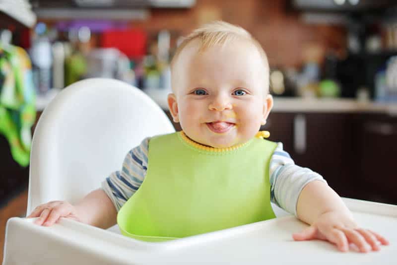 smiling baby boy sitting in a high chair with tongue out