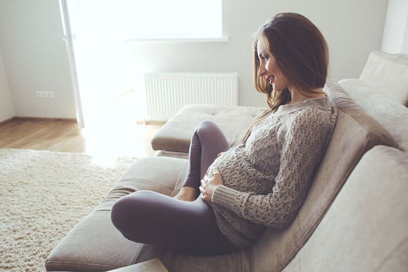 smiling pregnant woman feels the baby moving in belly while sitting on the couch