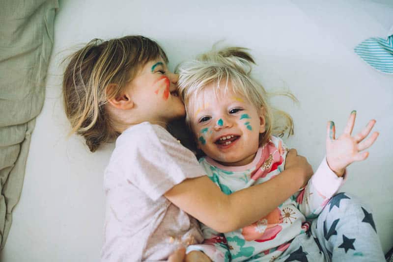 two little sisters with color on face laughing on the bed
