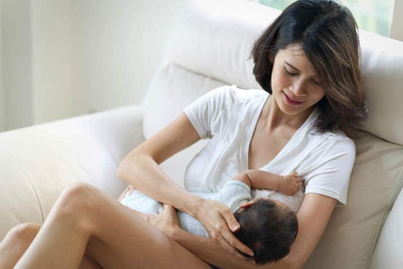 young mother breastfeeding her baby on the couch