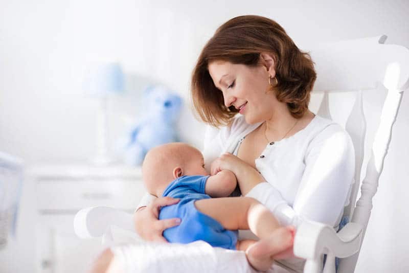 young mother sitting in nursing glider and breastfeeding her baby