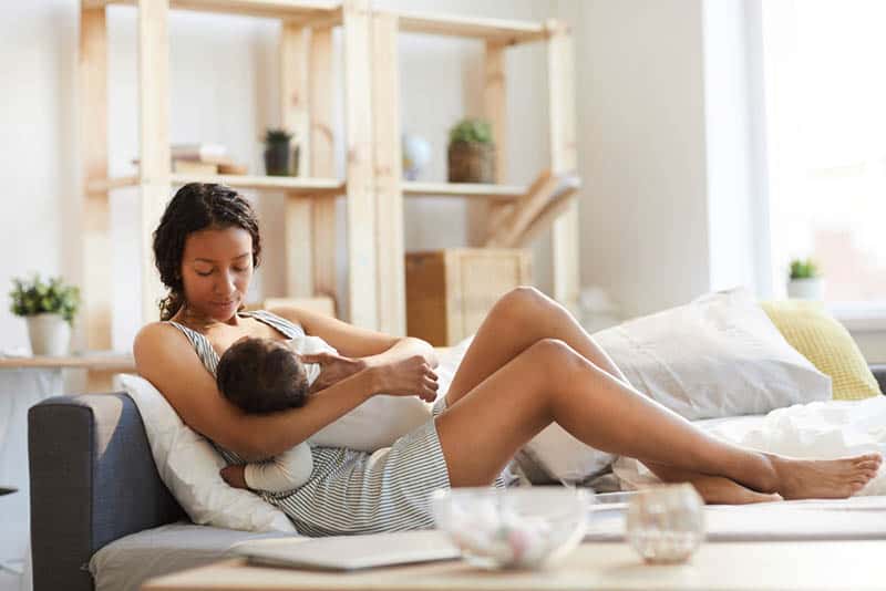 young mother sitting on sofa bed and breastfeeding her baby
