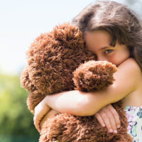 shy little girl hugging with her teddy bear