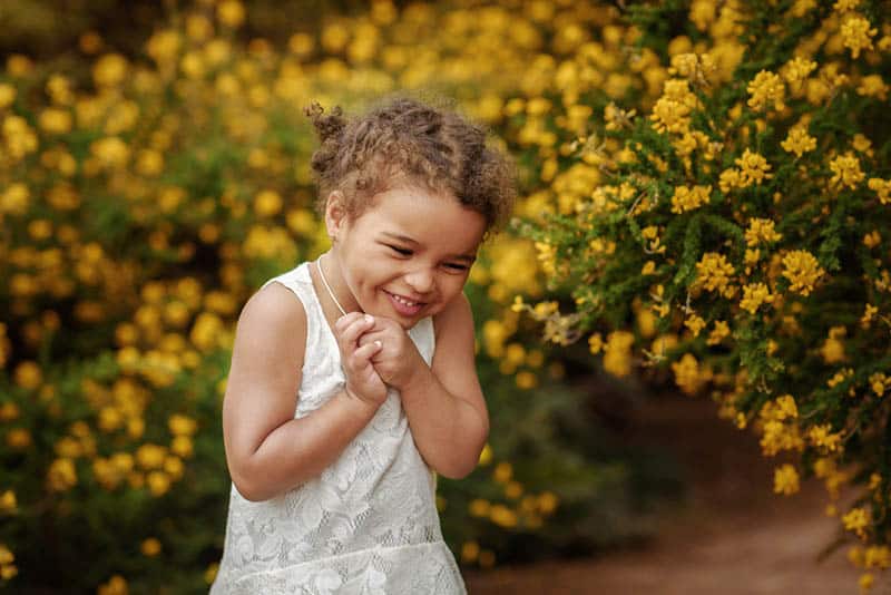 Happy little girl on the field of yellow flowers in summer