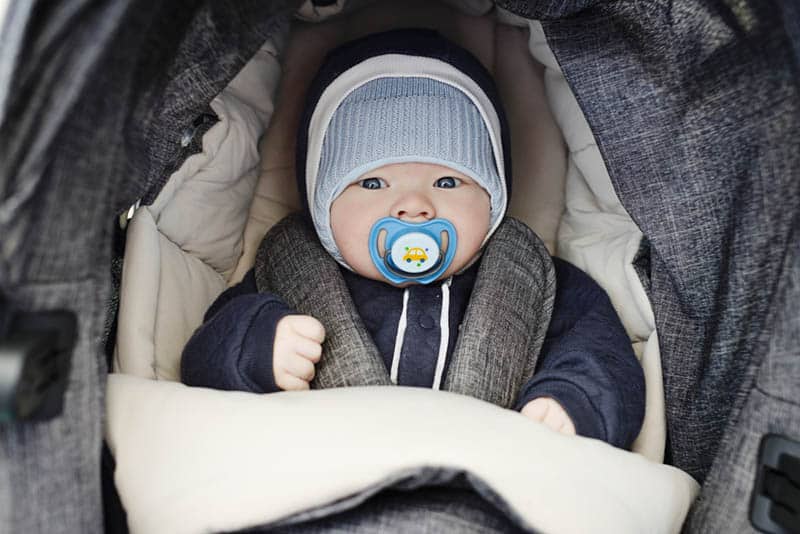 adorable baby boy with hat and winter clothes sitting in a stroller
