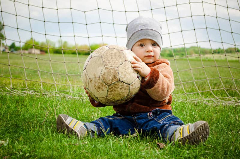 cute baby boy posing with football ball on the grass
