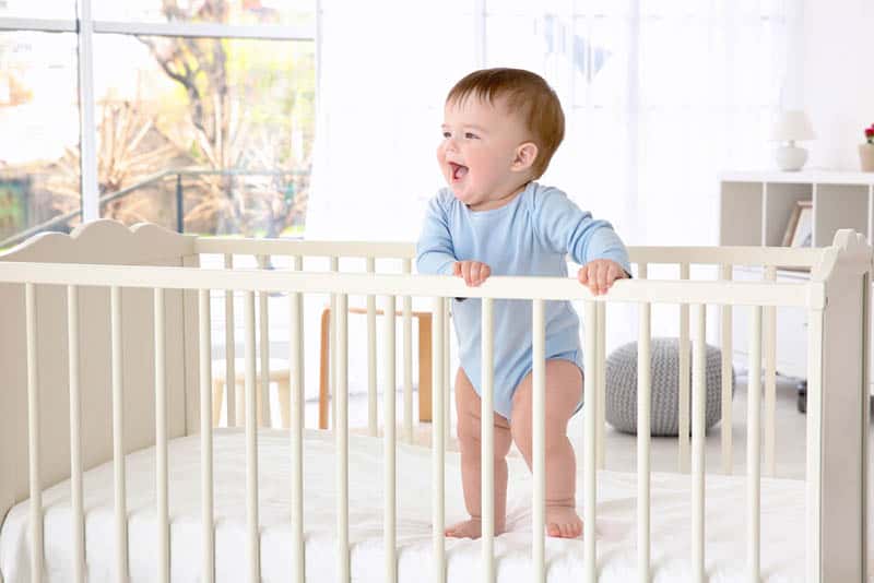 cute happy baby boy standing in the crib holding for rails
