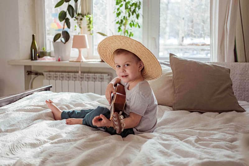 cute little boy holding a guitar on the bed