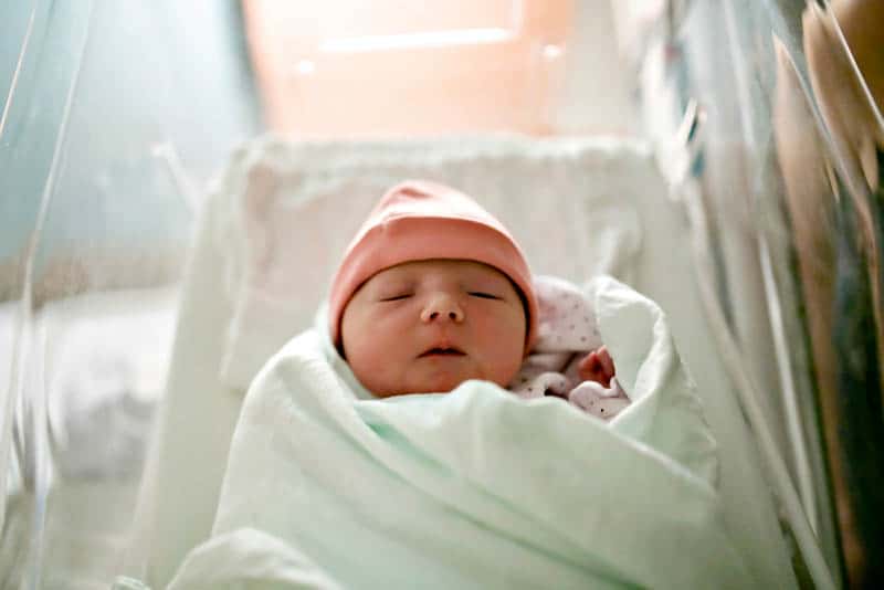 newborn baby with hat wrapped into blanket