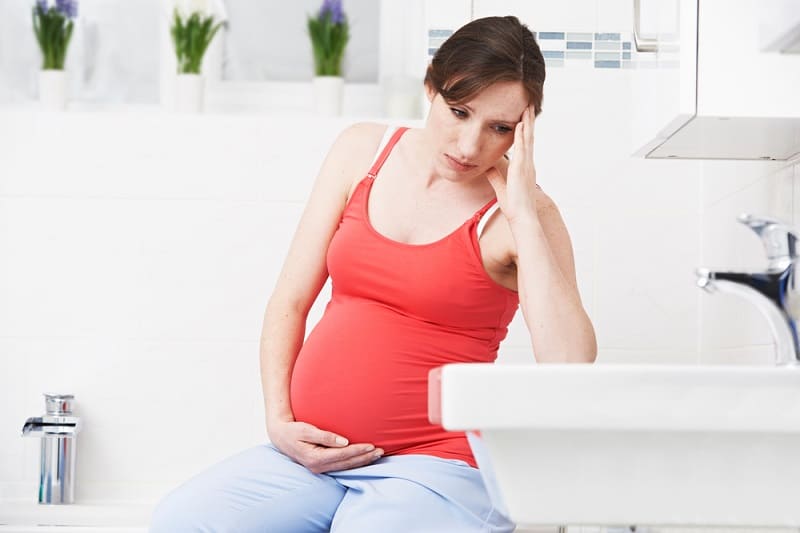 nauseous pregnant woman sitting in the bathroom and holding her belly