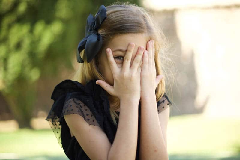 shy little girl covering face with hands outdoor