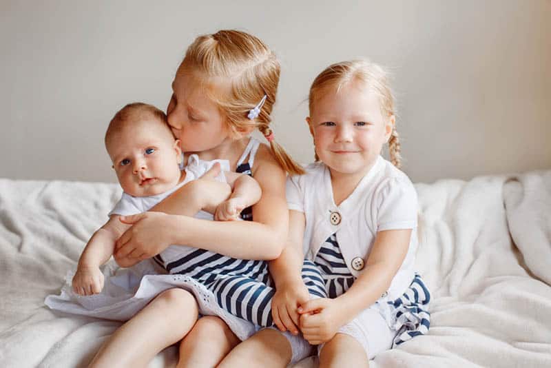sweet sisters sitting with baby brother and kissing him