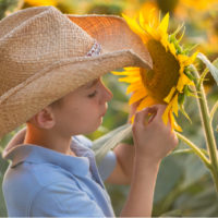 boy in a cowboy hat next to a sunflower