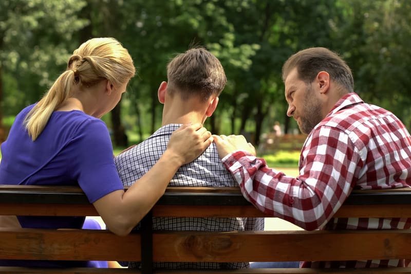 parents having a conversation with son on a bench